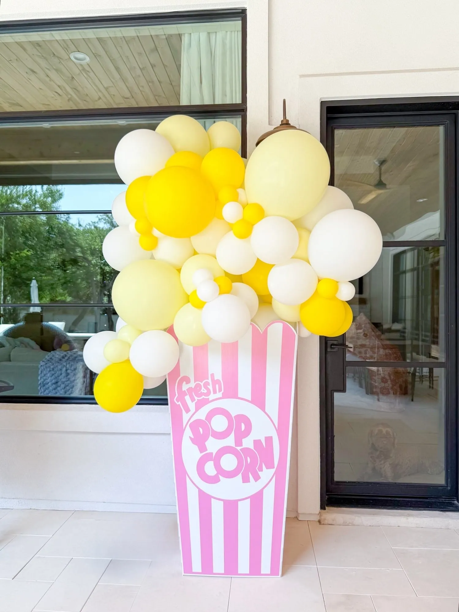 Giant pink striped popcorn box overflowing with yellow and white balloons