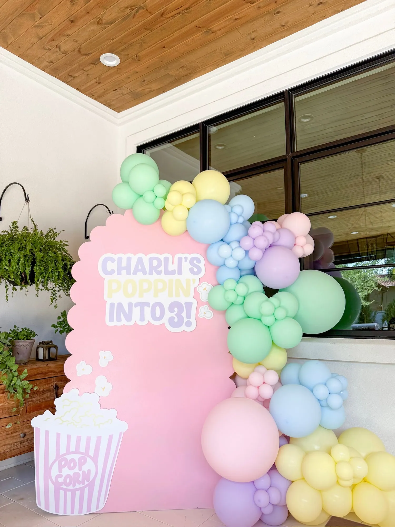 Popcorn themed third birthday with a pink scalloped backdrop and pastel rainbow balloon garland
