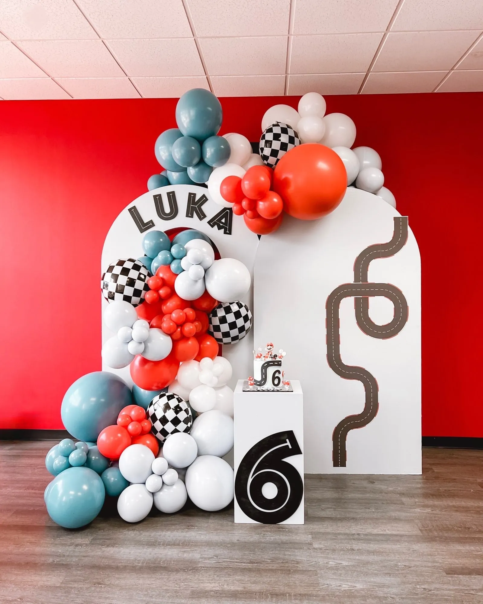 Race car themed sixth birthday with white arch backdrops, red, blue and checkered balloon garland and a cake pedestal