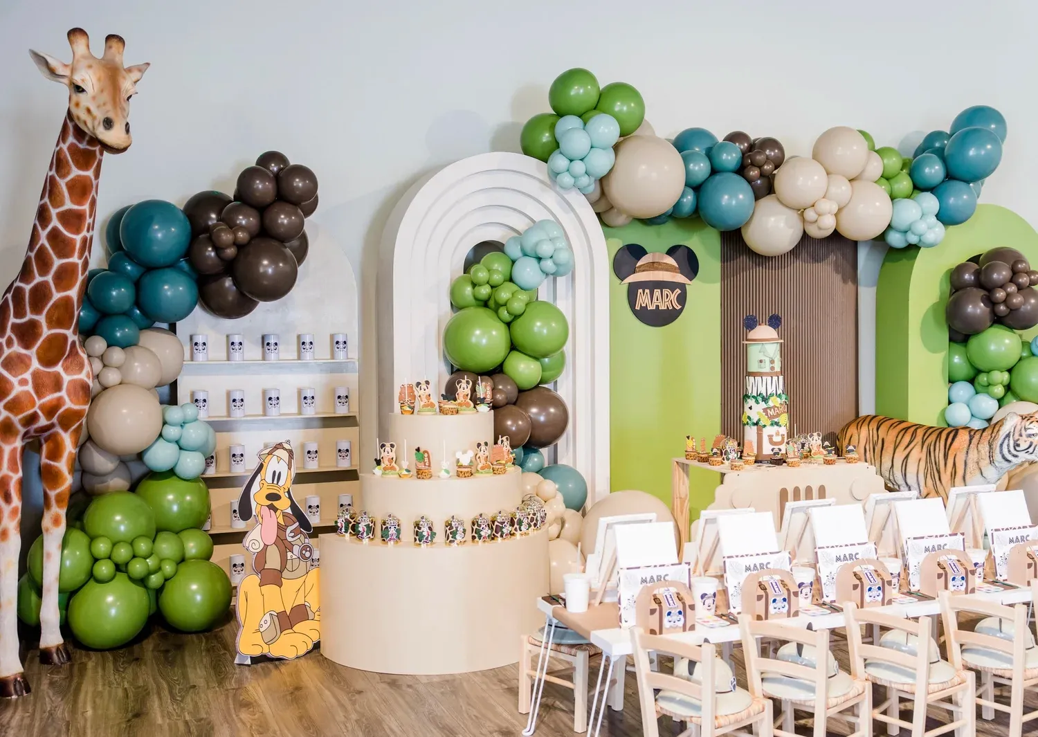 Safari birthday with green and brown balloon garland, arch backdrops, dessert display and kids table