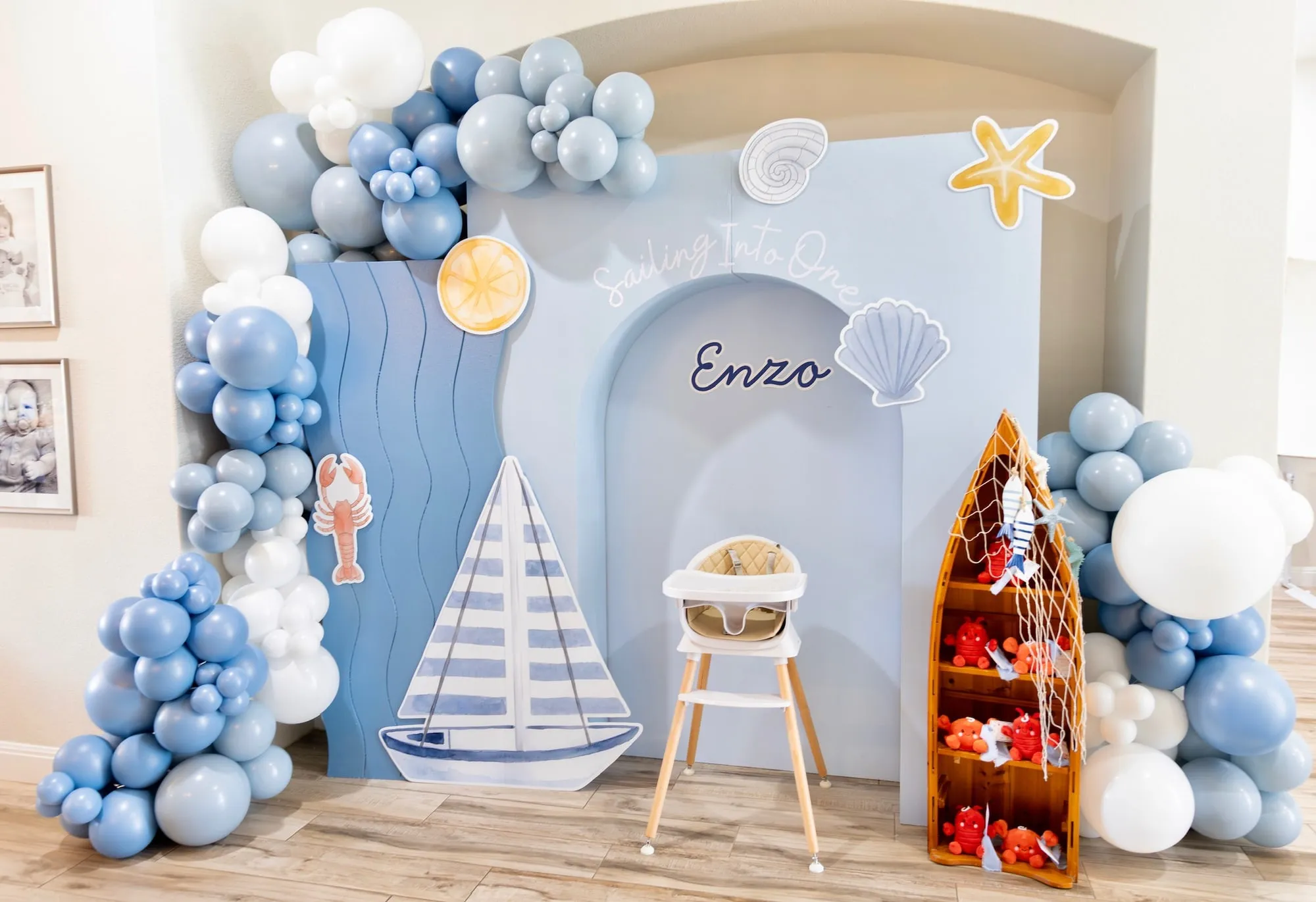 Sailing Into One nautical first birthday with blue arch backdrops, sailboat and shell cutouts, a boat shelf and dusty blue and white balloon garland