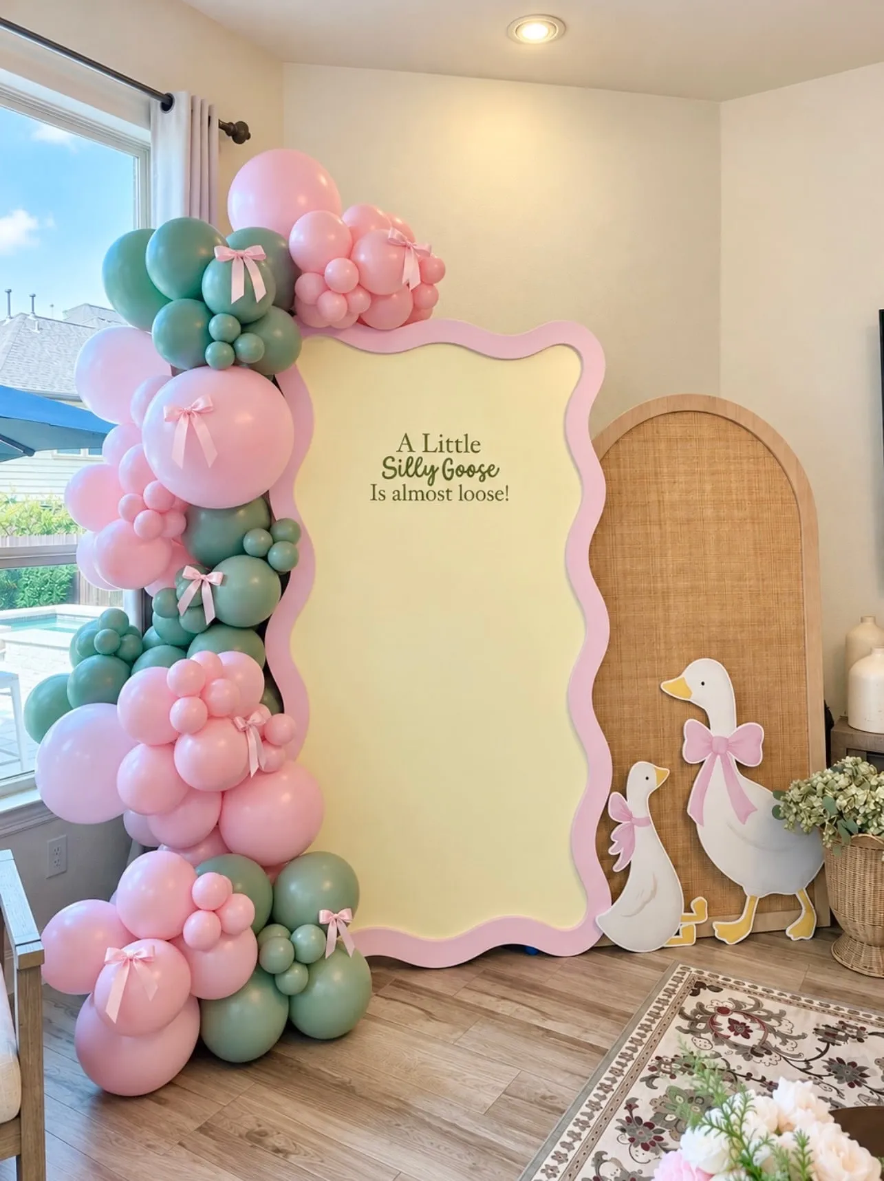 Silly goose baby shower with a pink wavy panel, rattan arch, goose cutouts and pink and sage balloon garland with bows