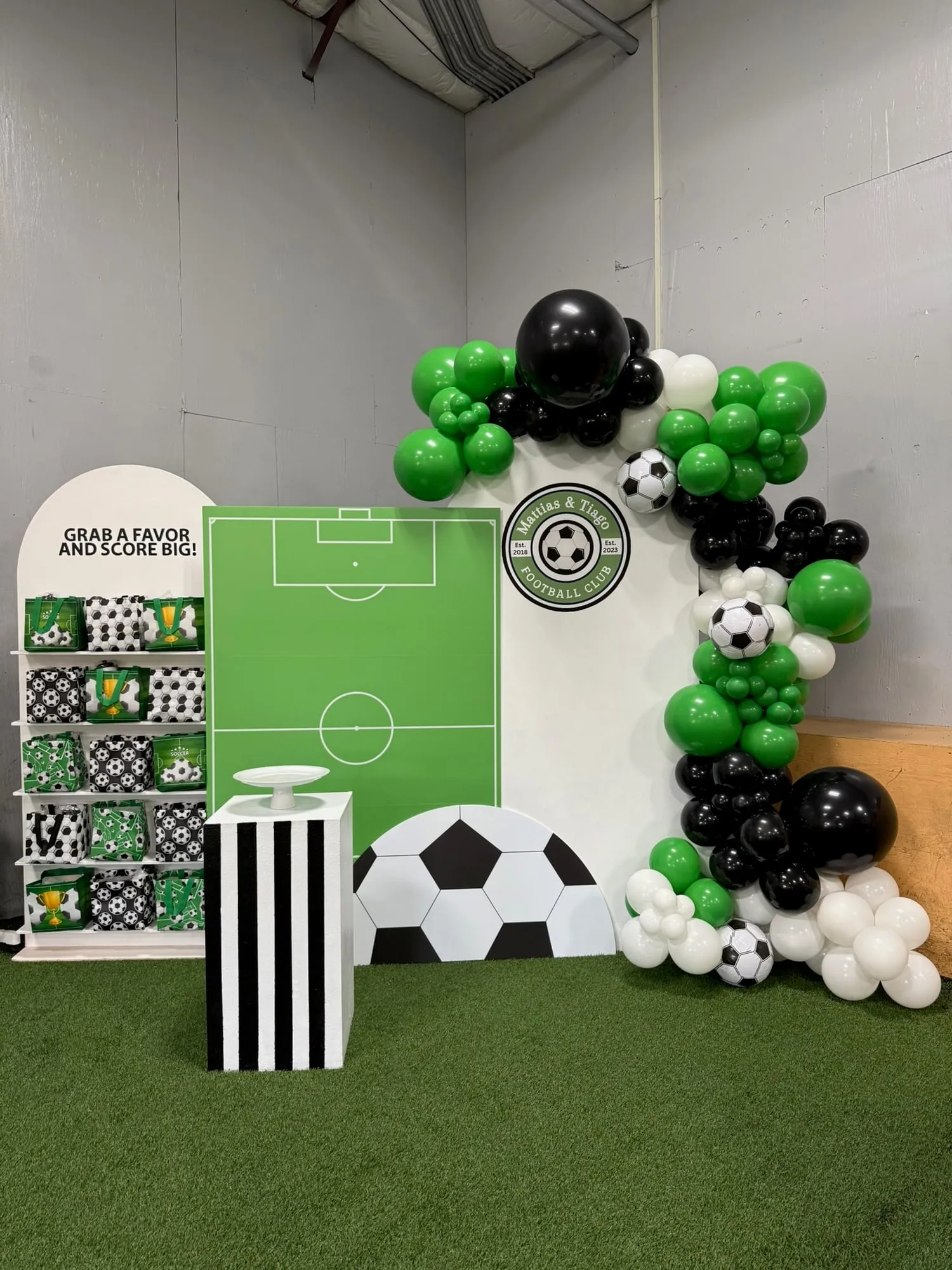 Soccer themed birthday with a field backdrop, favor shelf, soccer ball cutout and green, black and white balloon garland