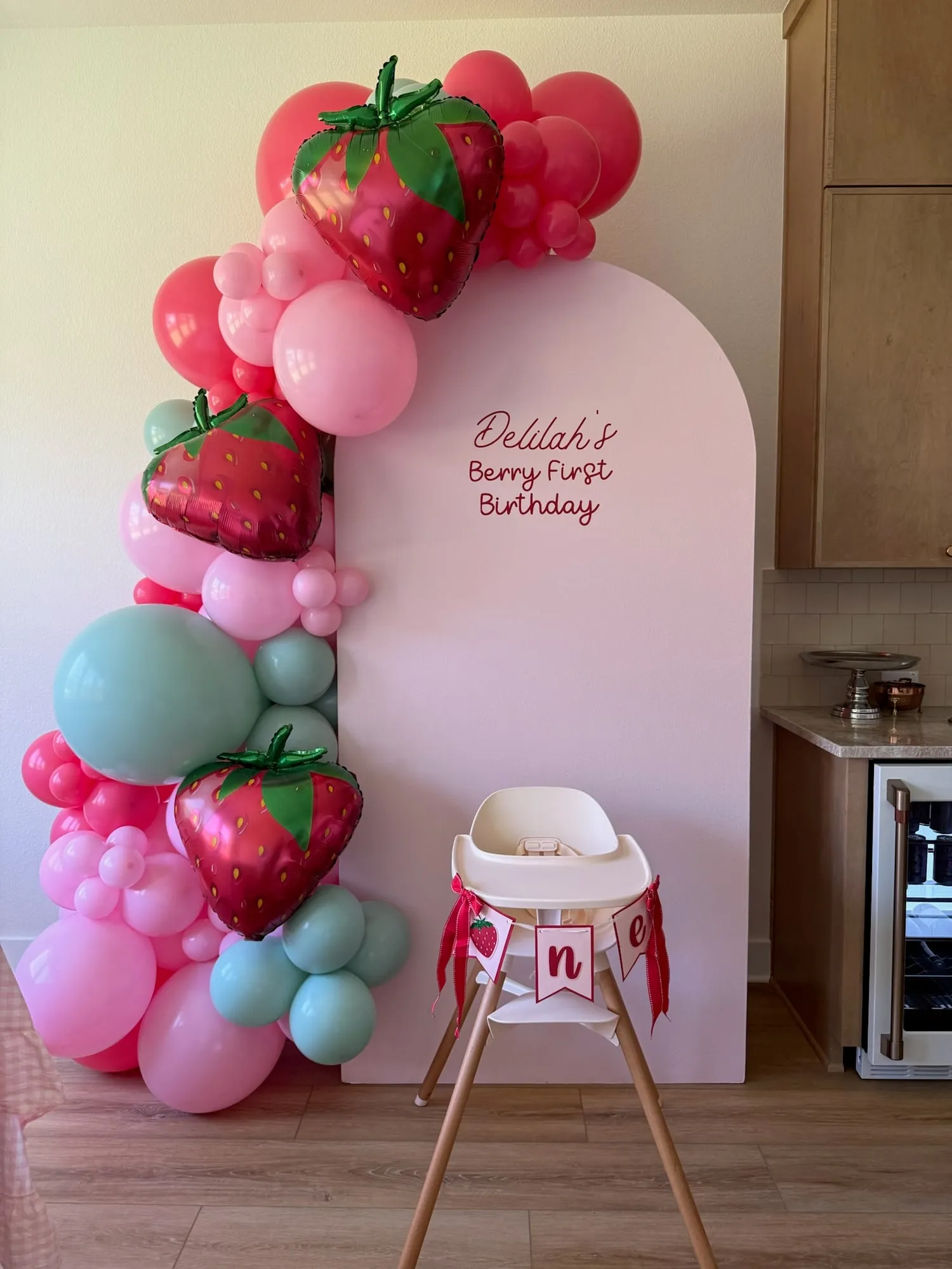 Berry First Birthday with a pink arch, strawberry balloons, pink and mint balloon garland and a high chair banner