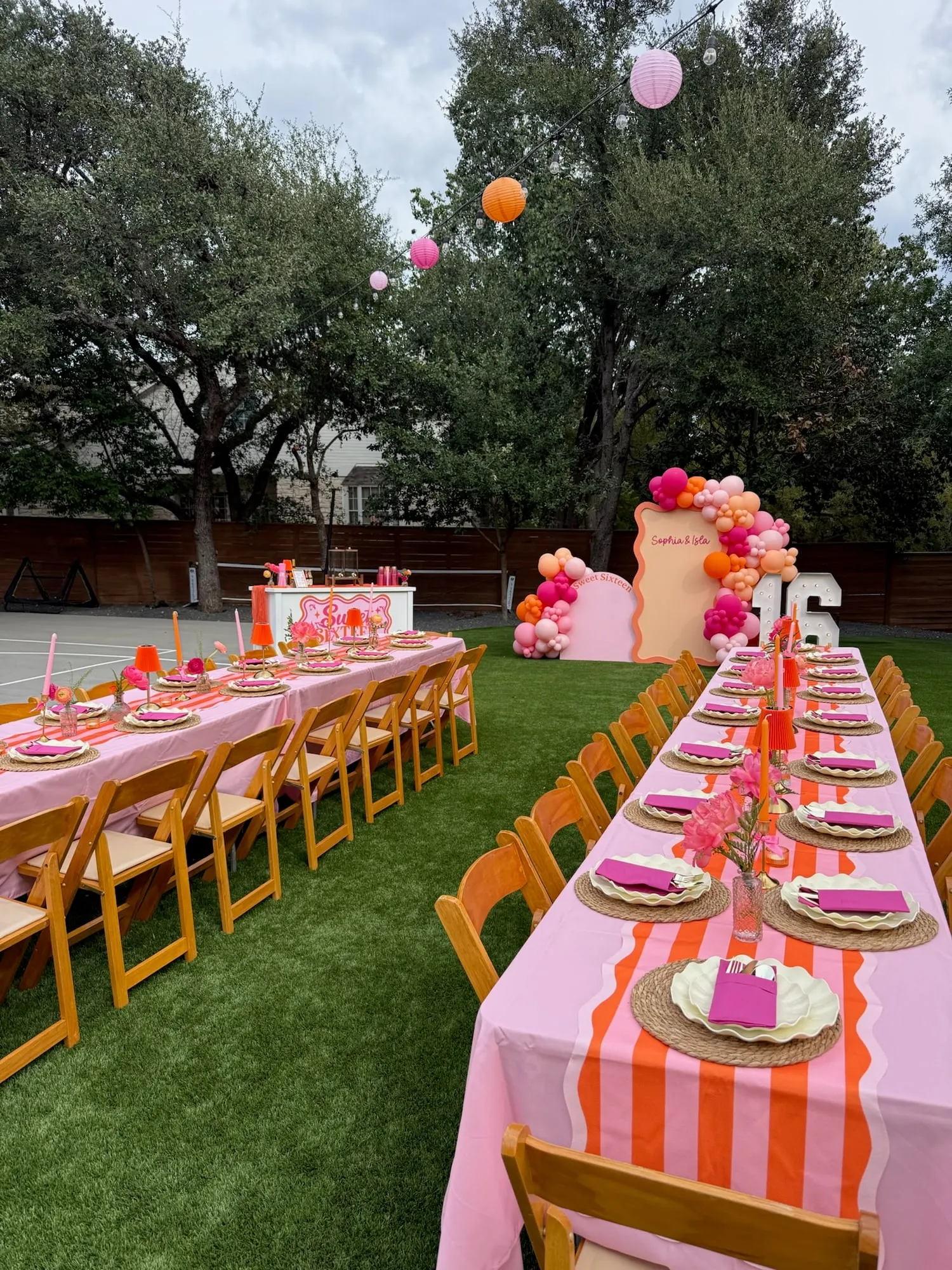 Sweet sixteen dinner with long pink and orange striped tables, wavy plates, taper candles and paper lanterns in a backyard