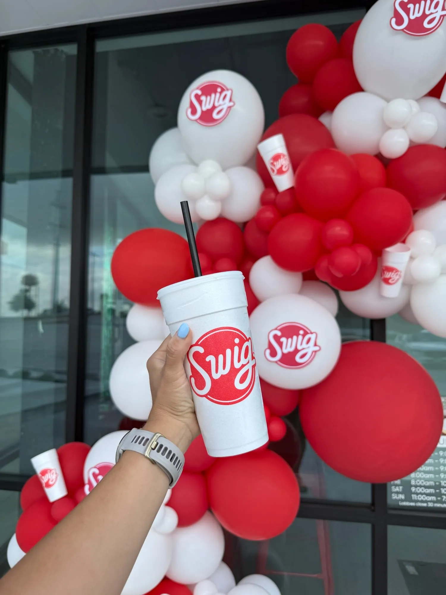 Swig cup held up in front of a red and white branded balloon garland
