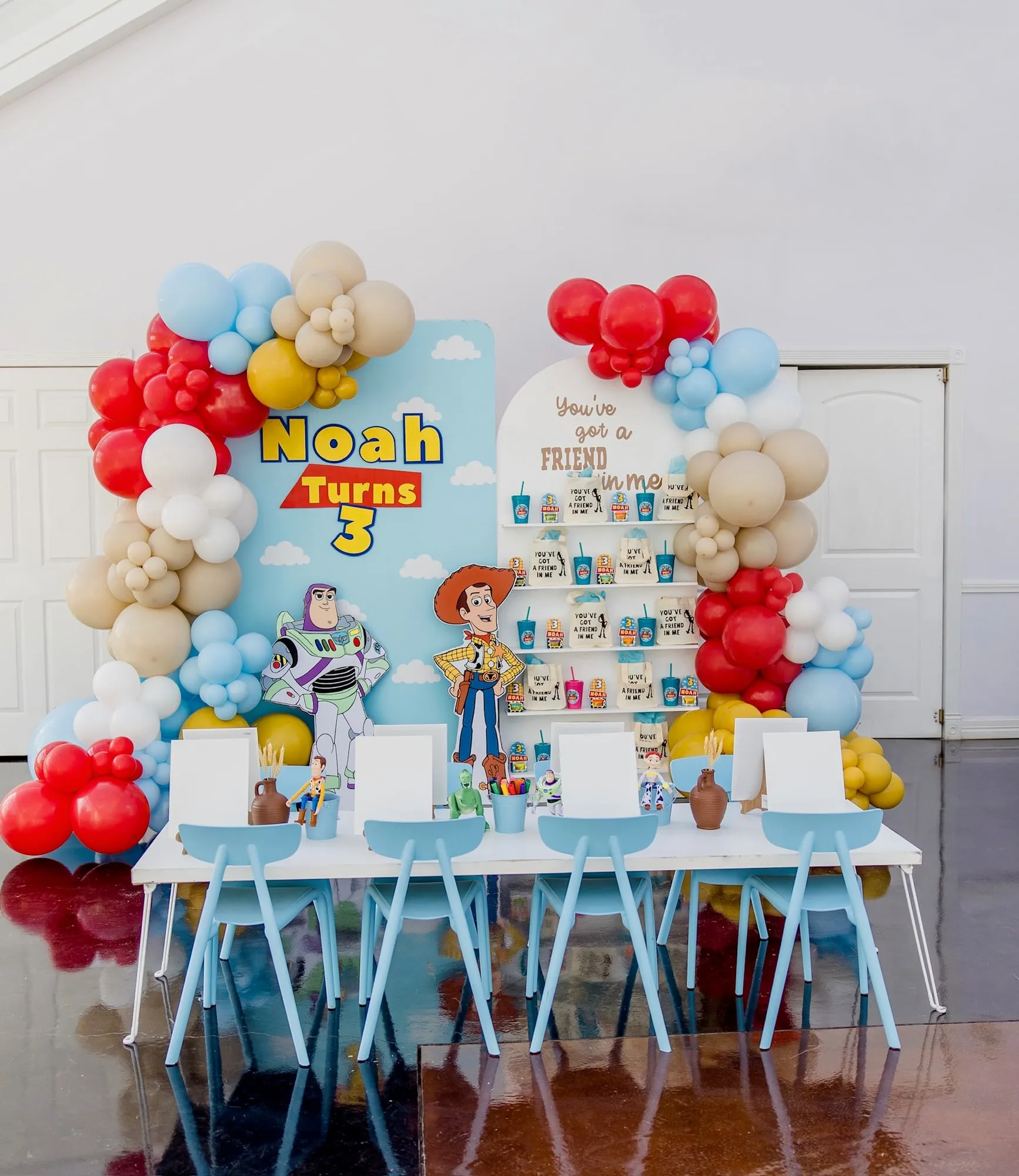 Toy Story themed third birthday with sky blue backdrop, red, blue and tan balloon garland, favor wall and styled kids table
