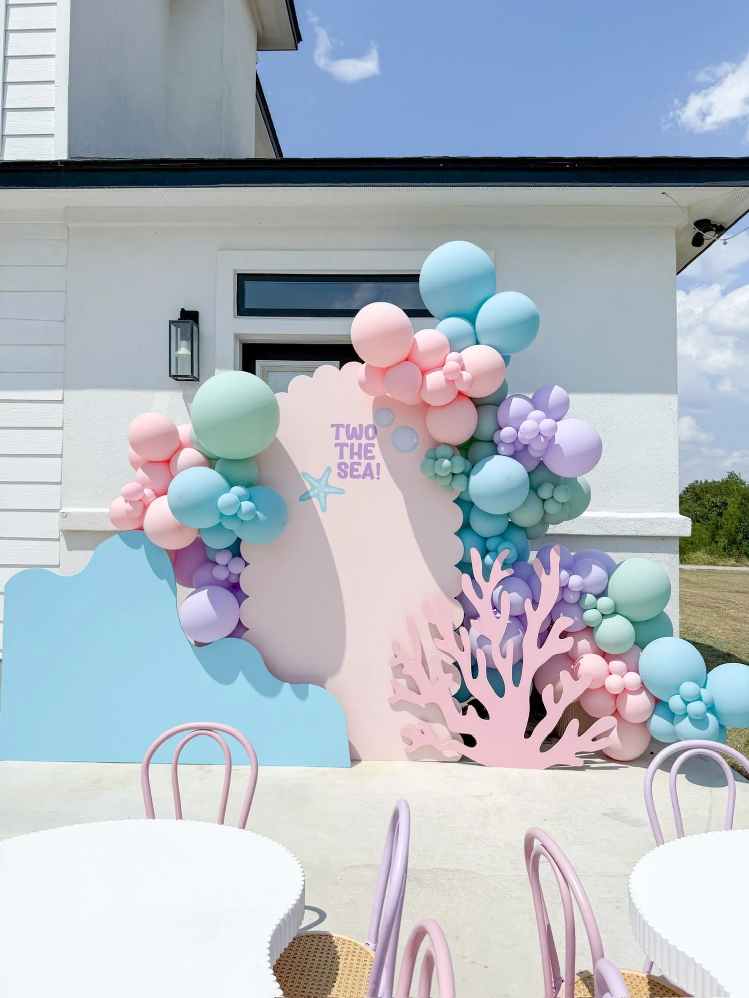 Under the sea second birthday with a pink scalloped backdrop, coral cutout and pastel balloon garland