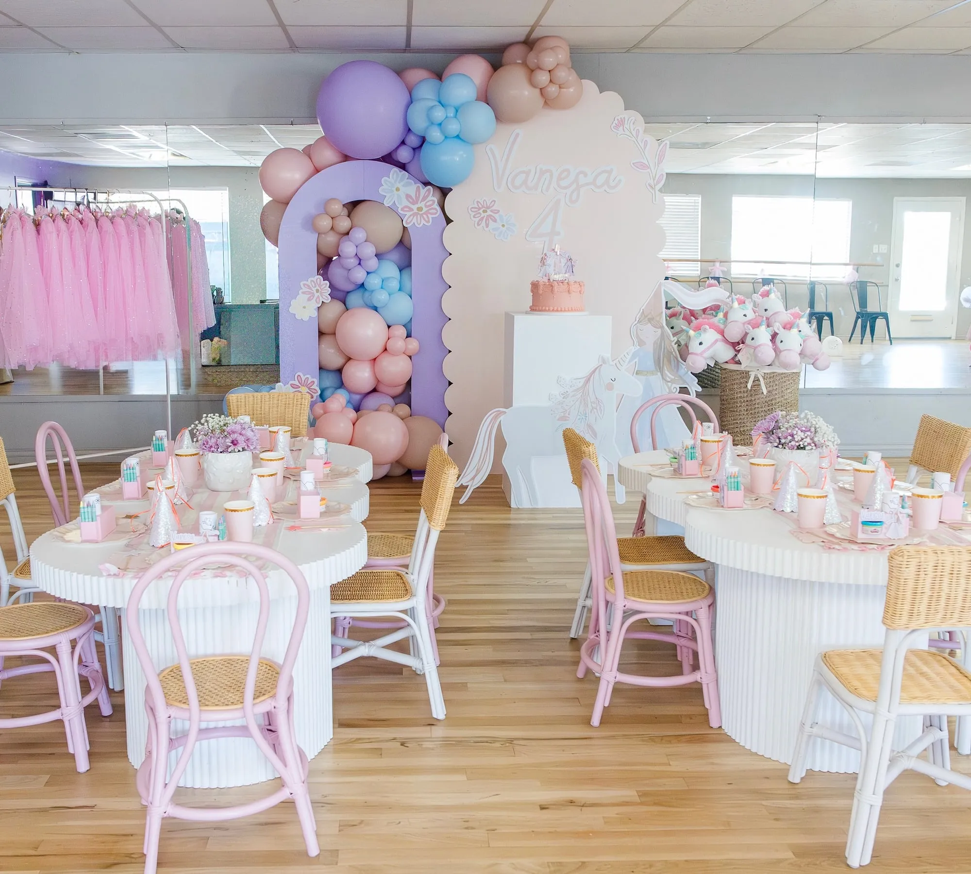 Unicorn themed fourth birthday in a dance studio with scalloped and lilac arch backdrops, pastel balloons and styled kids tables