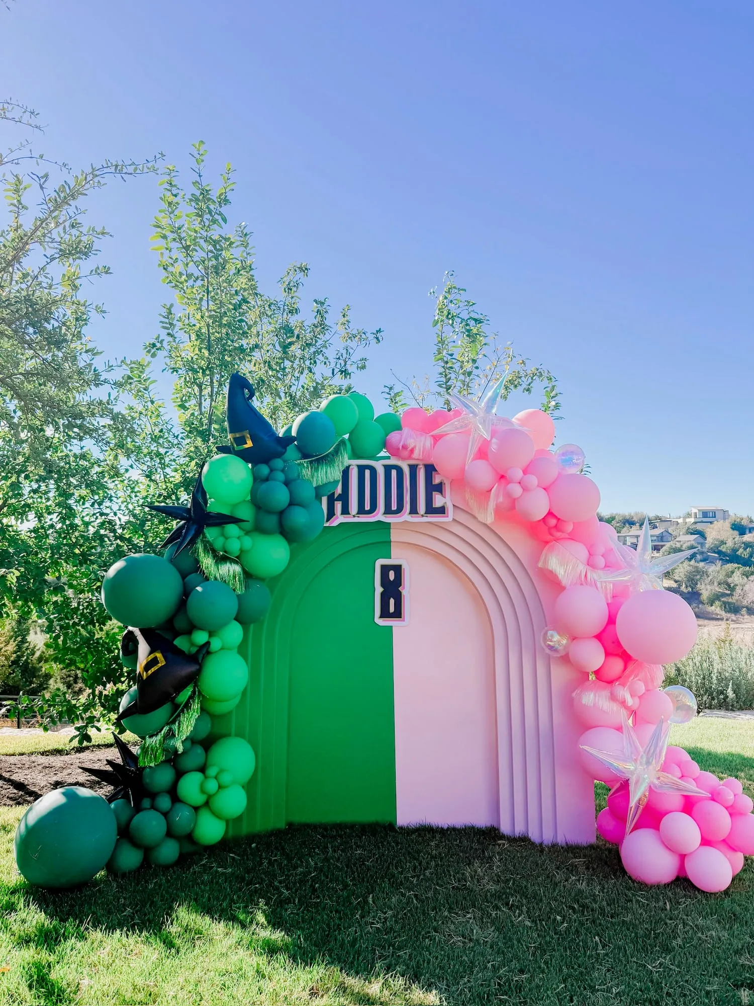 Wicked themed eighth birthday with a half green, half pink stepped arch, witch hat balloons, iridescent stars and fringe
